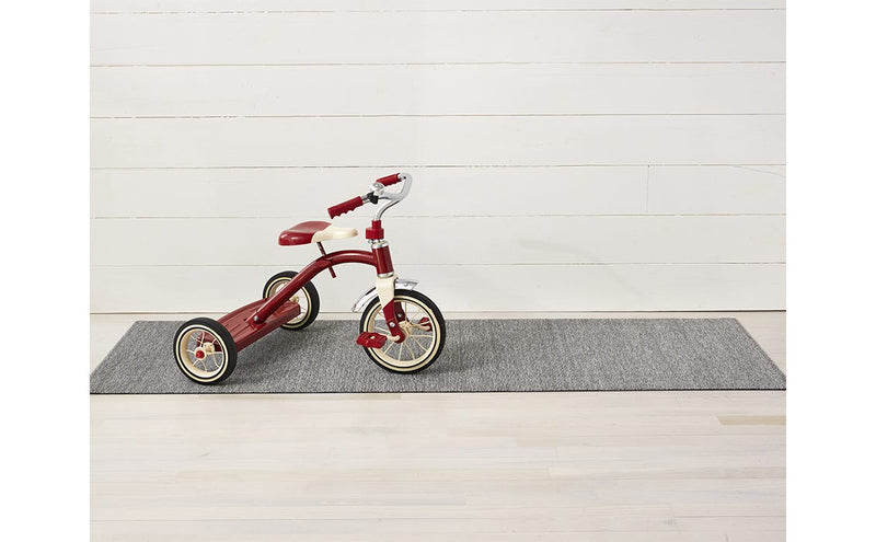 Red tricycle on a rug next to Chilewich Heathered Shag Mat in Fog, showcasing durable, quick-drying texture suitable for various spaces.
