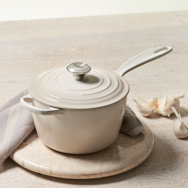 Le Creuset Signature Saucepan with lid on marble surface, ideal for sauces and grains, featuring ergonomic handles for easy maneuvering and exceptional heat retention.
