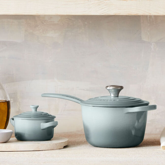 Le Creuset | Signature Saucepan displayed on a shelf among other kitchenware, emphasizing its smooth interior and ergonomic handles for versatile cooking needs.