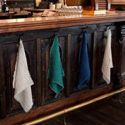 Sir|Madam Linen Frayed Edge Napkins, Curry, Set of 4, displayed on a wooden bar with hooks, showcasing their casual elegance and practical design.