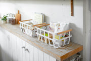 Yamazaki Home | Steel + Wood Storage Baskets, Large, on a kitchen counter, filled with packaged foods and kitchen linens, exemplifying organized storage.