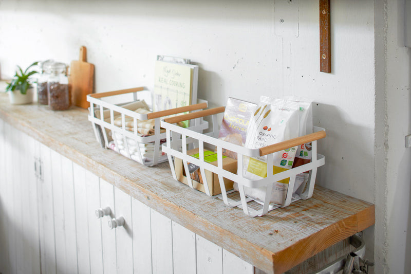Yamazaki Home | Steel + Wood Storage Baskets, Large, on a kitchen counter, filled with packaged foods and kitchen linens, exemplifying organized storage.