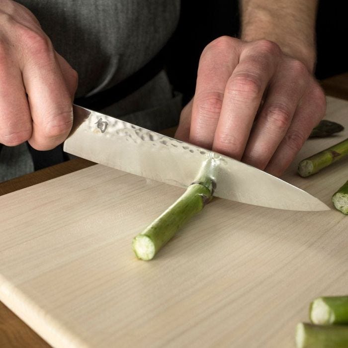 Hands slicing asparagus with the Shun | Premier Utility 6.5 Walnut knife, showcasing its precision and versatility, ideal for various kitchen tasks at Athens Cooks.