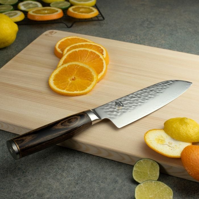Shun | Premier Santoku Walnut, 7 knife on a cutting board with citrus slices, showcasing its hammered finish and elegant handle, ideal for versatile kitchen tasks.