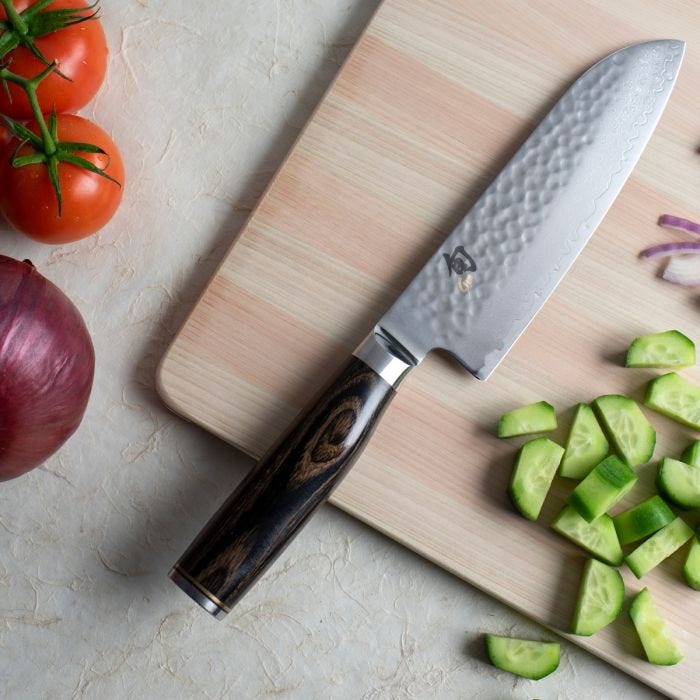 Shun | Premier Santoku Walnut, 7 knife on a cutting board with sliced cucumber, red onion, and tomatoes, showcasing its versatility for kitchen prep at Athens Cooks.