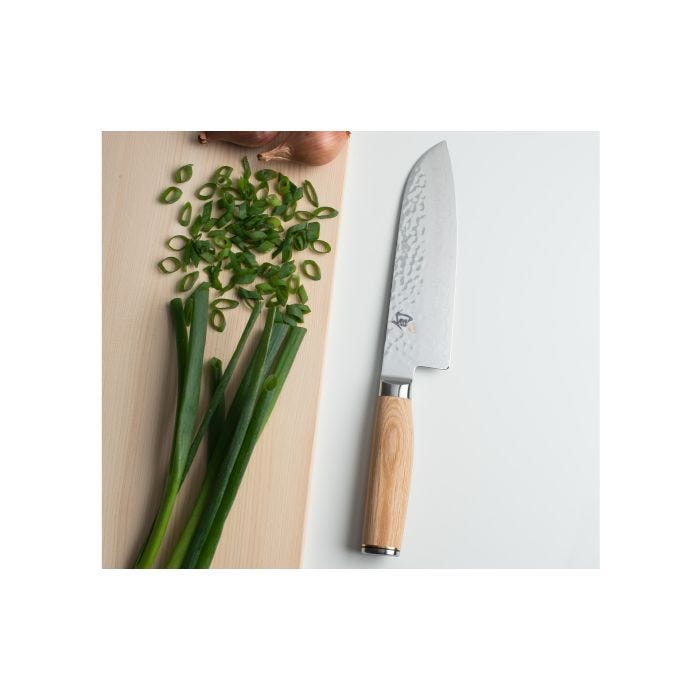 Shun | Premier Blonde Santoku, 7 knife with hammered blade and blonde Pakkawood handle, on a board with scallions and shallots, showcasing its versatility in kitchen tasks.