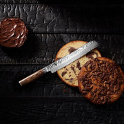 Shun Premier Bread Knife, 9, with a hammered finish and wood handle, alongside sliced marble cakes and chocolate frosting on a dark wood surface.