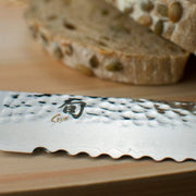 Shun Premier Bread Walnut, 9 knife with serrated blade and Damascus pattern on a cutting board, ideal for slicing whole-grain bread without crushing or tearing.