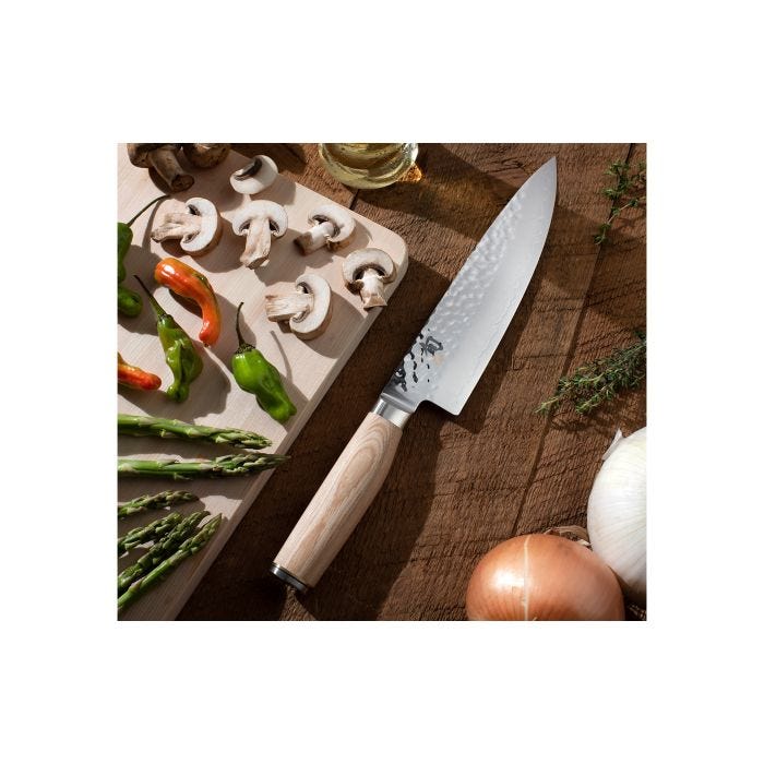 Shun | Premier Blonde Chef's Knife, 8 inches, with a hammered-finish blade, rests on a wooden surface amidst fresh vegetables, showcasing its precision and elegance.
