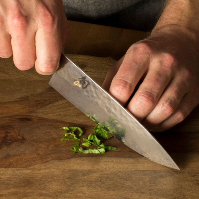 Hands using Shun | Premier Chef's Knife, 6 inches, to finely slice basil on a wooden board, showcasing its nimble, precise performance for culinary tasks.