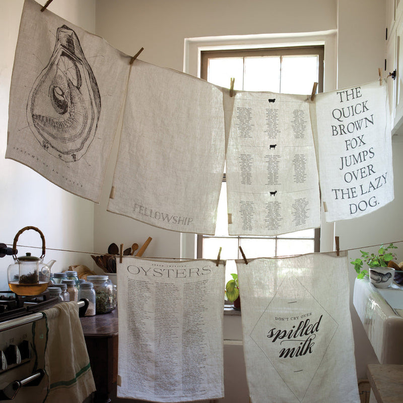 Sir|Madam Linen Tea Towels, featuring a detailed list of North American oysters, hang in a cozy vintage-style kitchen corner, perfect for drying fine china.