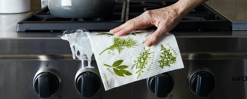 A hand holds Three Bluebirds Swedish Dishcloths over a stove, illustrating their durability and eco-friendly design, ideal for kitchen cleaning tasks.