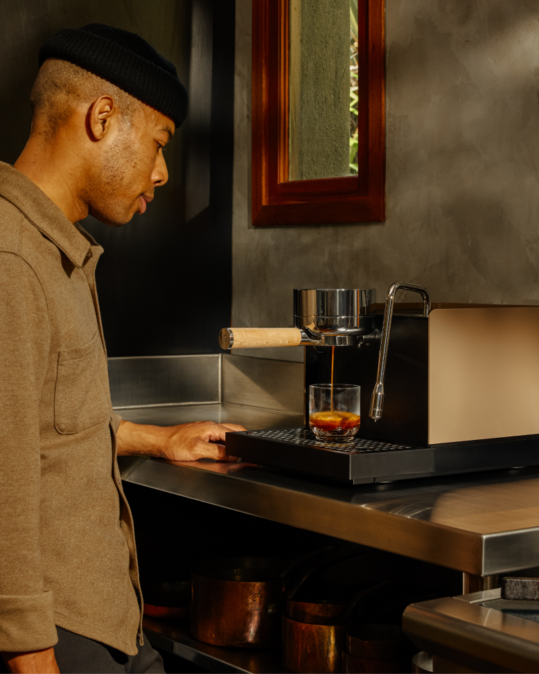 Man observes espresso pouring into a glass from FELLOW | Espresso Series 1, exemplifying professional home performance, in a kitchen setting.