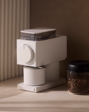 FELLOW | Ode Brew Grinder Gen 2, Matte White on countertop with coffee beans. Features large dial, catch cup, offers precise grind for optimal coffee brewing.