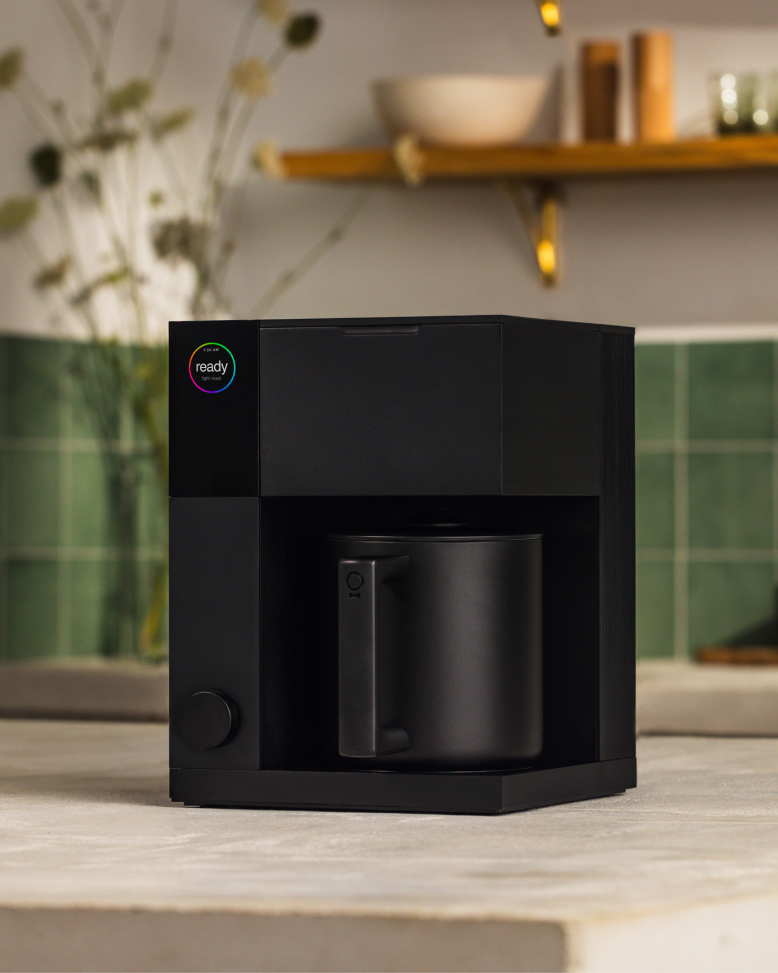 FELLOW | Aiden Precision Coffee Maker, Matte Black on countertop with mug, offering automated pour-over brewing for perfect coffee every time.