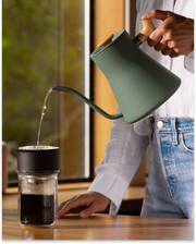 A person pours water with the FELLOW | Stagg EKG Pro Electric Kettle into a dripper, brewing coffee into a Fellow glass carafe.