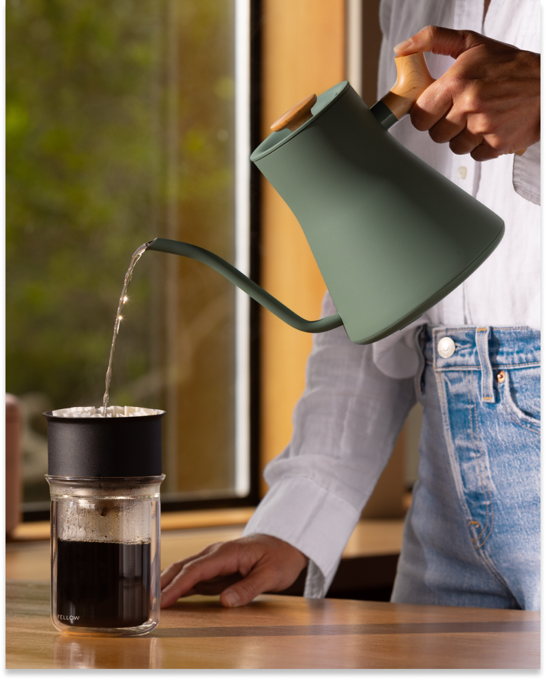 A person pours water with the FELLOW | Stagg EKG Pro Electric Kettle into a dripper, brewing coffee into a Fellow glass carafe.