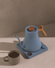 FELLOW | Stagg EKG Pro Electric Kettle in Hazy Blue with Maple handle on a countertop, showcasing precise temperature control for perfect pour-over coffee.