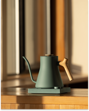 FELLOW | Stagg EKG Pro Electric Kettle, Smoke Green w/ Maple, on base; precision pour-over spout, wooden handle, ideal for coffee enthusiasts seeking control and style.