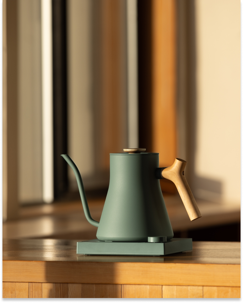 FELLOW | Stagg EKG Pro Electric Kettle, Smoke Green w/ Maple, on base; precision pour-over spout, wooden handle, ideal for coffee enthusiasts seeking control and style.