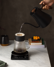 FELLOW | Stagg EKG Pro Electric Kettle, Stone Blue w/ Walnut, pours into a dripper over a carafe on a digital scale, embodying precision brewing.