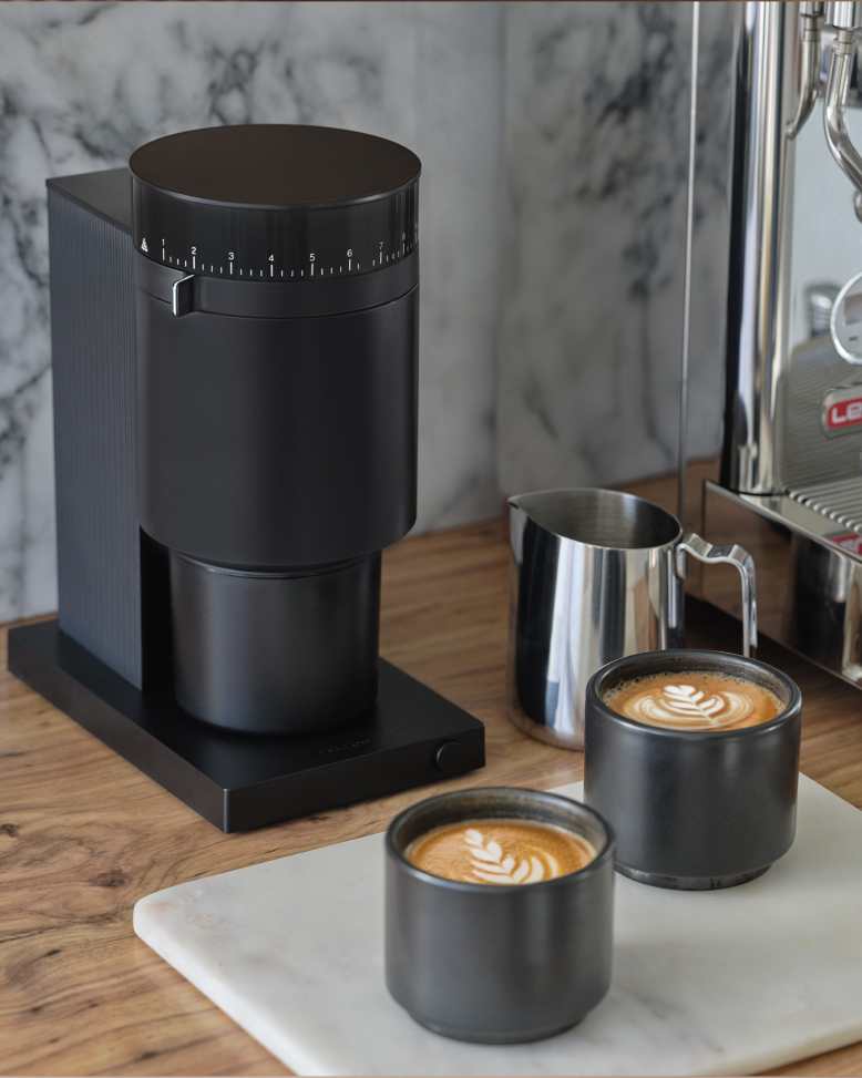 FELLOW | Opus Conical Burr Grinder, Matte Black, on a kitchen countertop with espresso machine, milk pitcher, and espresso cups showcasing its versatility for various brewing styles.