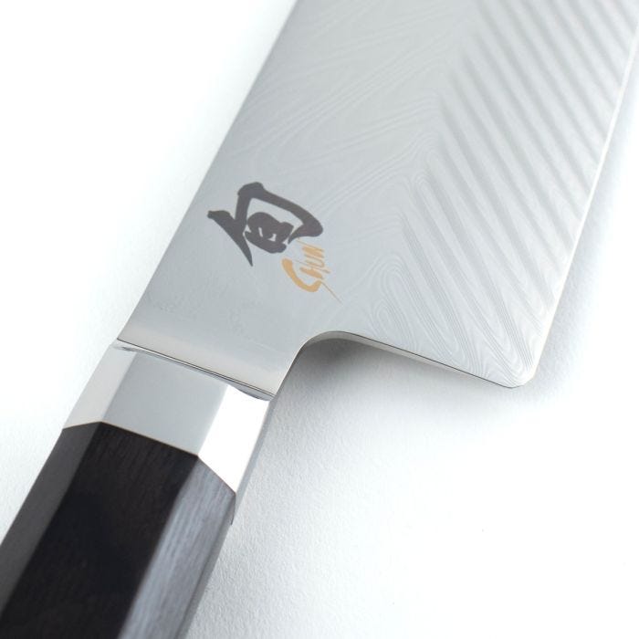 Close-up of Shun Dual Core Santoku, 7 inches, featuring a Damascus steel nakiri blade, polished bolster, and octagonal dark-wood handle with stamped kanji mark.