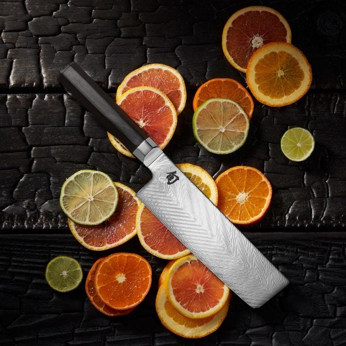 Shun Dual Core Nakiri, 6.5 inches, showcased on charred wood with citrus slices, exemplifies craftsmanship and precision for versatile vegetable and fruit preparation.