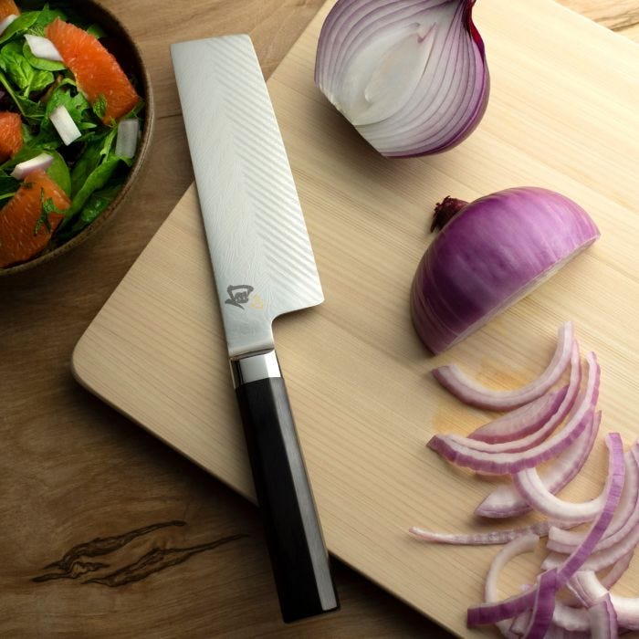 Shun Dual Core Nakiri, 6.5 inches, displayed with sliced onion, a wooden handle, and a patterned blade on a cutting board, showcasing its vegetable slicing precision.