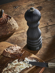 Peugeot | Paris Nature Collection Pepper Mill, Nature Black, on a rustic table with sliced bread and cheese, embodying eco-friendly craftsmanship for culinary excellence.