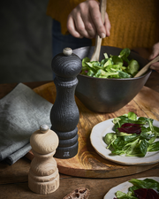 Peugeot | Paris Nature Collection Pepper Mill, Nature Black, showcased on a rustic table with salad, highlighting eco-friendly design and lifetime-guaranteed mechanism amidst a kitchen scene.