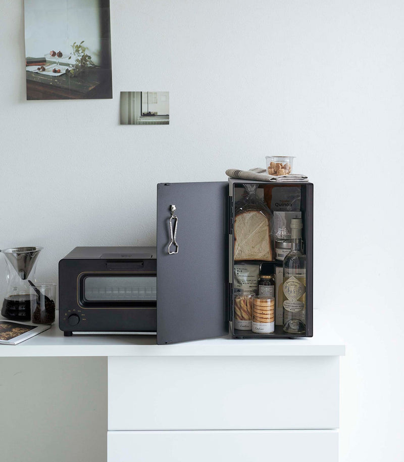 Yamazaki Home | Bread Box, Vertical, Steel, Black neatly stores bread and snacks beside a tidy kitchen setup with a toaster-oven and pour-over coffee setup.