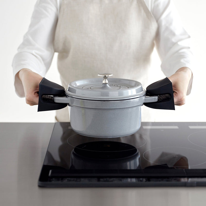 Person uses Yamazaki Home Magnetic Pot Holders, Silicone, Black, to safely lift a lidded grey pot from an induction cooktop.