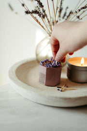 Tenn Prairie Match Holders with Striker: A close-up of a hand holding a blue concrete match holder with cork bottom, featuring included matches and striker pad.