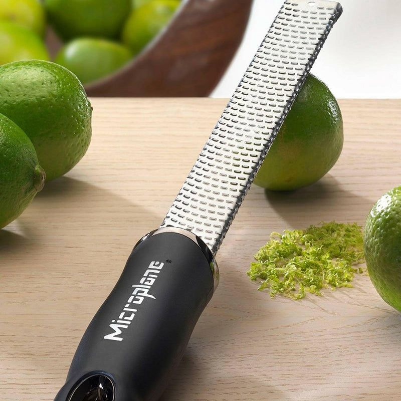 Microplane | Premium Zester, Grater - Classic Blue, shown resting on wood with limes and zest, ideal for effortless citrus zesting and grating in culinary settings.