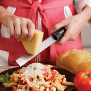 Close-up of a Microplane Premium Zester grating Parmesan over penne pasta, showcasing its precise, effortless grating capabilities.