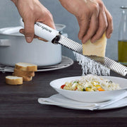 Microplane Premium Zester, Grater - Classic Blue grates Parmesan over risotto, showcasing its precision on a dark wood table with kitchen essentials.