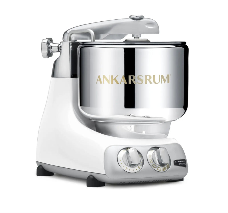 Ankarsrum Assistent Original stand mixer with polished stainless-steel bowl on a white base, featuring control knobs for speed and timer settings.