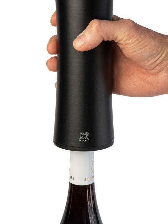 Hand holding Peugeot | Elis Reverse Rechargeable Electric Corkscrew - Natural, positioned over a wine bottle neck, showcasing its automatic uncorking capability.