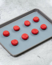 GIR | Baking Mat - Sprinkles - 12 x 17 displayed with red cookies, showcasing its use in baking on a kitchen counter.
