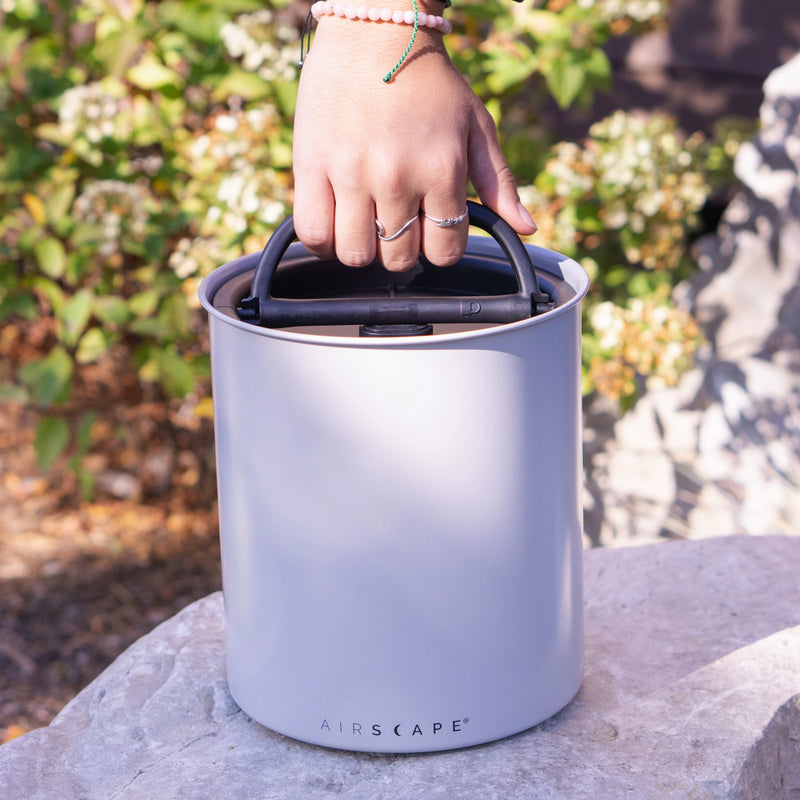 Close-up of a hand holding the Planetary Design | Airscape | Classic and Kilo Stainless Steel Canister, showcasing its durable and sleek design for preserving kitchen goods.