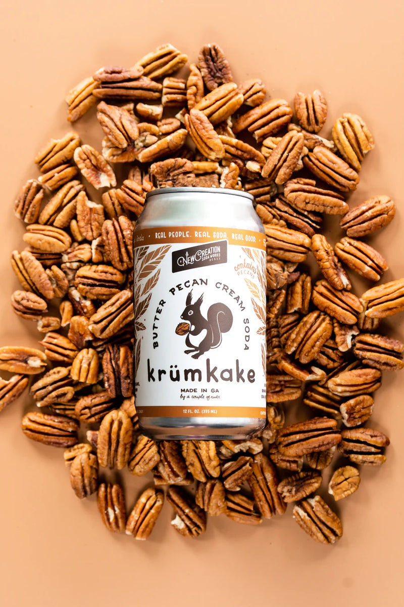 New Creation Soda Works' Krümkake Butter Pecan Cream Soda can, showcased with pecans, embodies creamy, buttery flavors inspired by Swedish pastry.