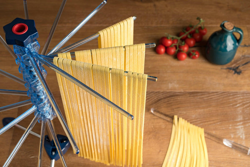Marcato | Tacapasta Pasta Drying Rack holding freshly cut tagliatelle, with cherry tomatoes and a ceramic jug in the background on a wooden countertop.